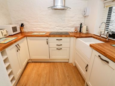 A kitchen with wooden countertops white cabinets a sink a stovetop a microwave and a toaster at Bay Tree Cottage in West Looe