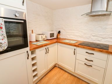 A kitchen corner with white cabinets wooden countertops a built in oven a toaster a microwave a knife block and a stovetop at Bay Tree Cottage in West Looe
