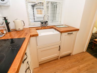 A kitchen corner with a white sink under a window with blinds and wooden countertops at Bay Tree Cottage in West Looe