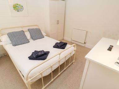 A bedroom with a metal bed frame two patterned pillows folded towels white wardrobe and a white dresser at Bay Tree Cottage in West Looe