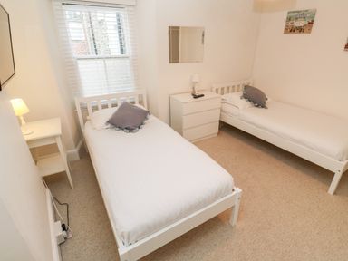 A bedroom with two single beds a small white table with a lamp a white dresser with a lamp and a window at Bay Tree Cottage West Looe