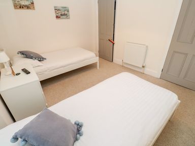 A bedroom with two single beds a bedside table with a lamp and remote control two paintings on the wall at Bay Tree Cottage in West Looe