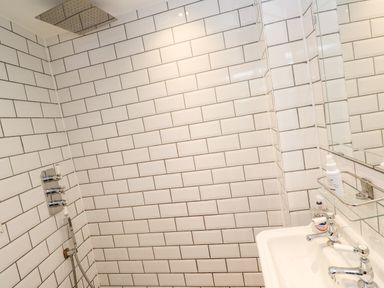 A bathroom with a showerhead a sink with faucet handles and toiletry bottles on a shelf at Bay Tree Cottage in West Looe