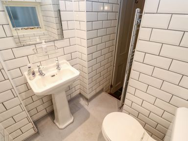 A bathroom with a pedestal sink a mirror a soap dispenser a toilet and white tiled walls at Bay Tree Cottage West Looe