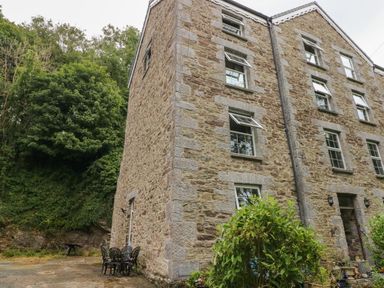 A stone building with multiple windows and outdoor chairs on a patio next to greenery at The Old Mill in Neyland near Milford Haven