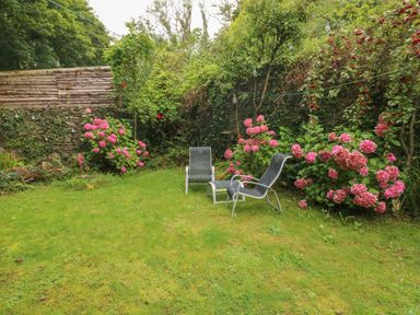 A garden with two chairs a small table and pink flowers along the stone and wooden fences at The Old Mill in Neyland near Milford Haven