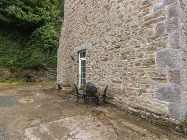 An outdoor area with a stone wall building a metal table and chairs and potted plants at The Old Mill in Neyland near Milford Haven