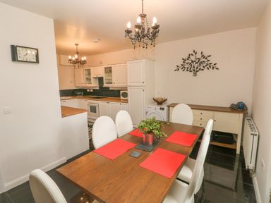 A dining area with a wooden table and white chairs next to a kitchen with white cabinets and black tiled floor at The Old Mill in Neyland near Milford Haven