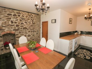 A dining area with a wooden table and white chairs next to a kitchen with wooden countertops and white cabinets at The Old Mill in Neyland near Milford Haven
