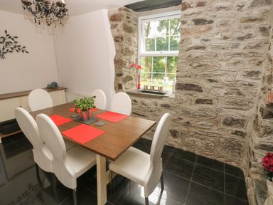 A dining room with a wooden table six white chairs and a window in a stone wall at The Old Mill in Neyland near Milford Haven