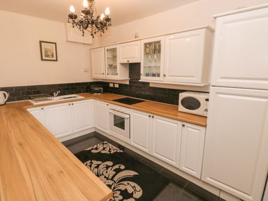 A kitchen with white cabinets wooden countertops a stove microwave black chandelier and a black and white rug at The Old Mill in Neyland near Milford Haven
