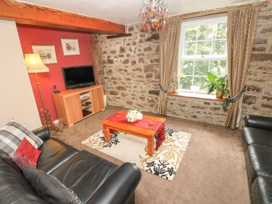 A living room with two black leather sofas a wooden coffee table on a patterned rug a television on a wooden stand a floor lamp and a window with curtains at The Old Mill in Neyland near Milford Haven