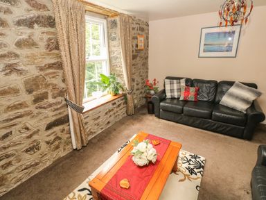 A living room with stone walls a window with curtains a black sofa and a wooden coffee table with flowers at The Old Mill in Neyland near Milford Haven
