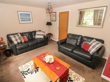 A living room with two black leather sofas a wooden coffee table with flowers on it a mirror on the wall and a wooden door at The Old Mill in Neyland near Milford Haven