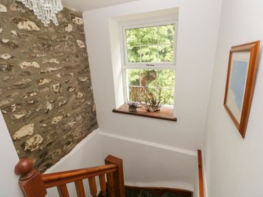 A stairway with wooden railing a stone accent wall a window with two decorative sea fans and a framed picture on a white wall at The Old Mill in Neyland near Milford Haven