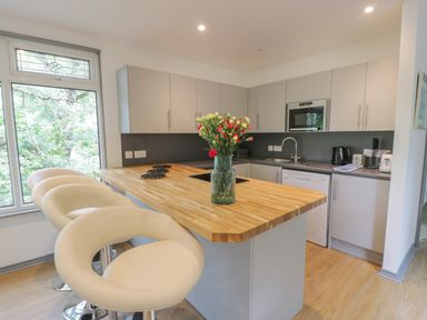 A kitchen with white bar stools and a wooden island countertop with flowers at The River Lodge in Oban