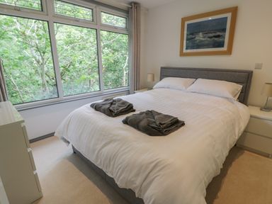 A bedroom with a bed covered in white linens near large windows showing green trees at The River Lodge in Oban