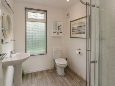 A bathroom with a sink, toilet, shower, window, and wall cabinet at The River Lodge in Oban