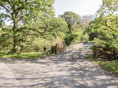 A gravel driveway with wooden gates and stone walls surrounded by trees at The River Lodge in Oban