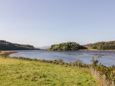 A river with grassy fields and trees along the banks at The River Lodge in Oban