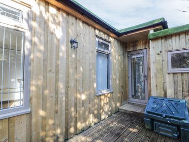 An outdoor wooden deck area with a glass door window and storage box at The River Lodge in Oban