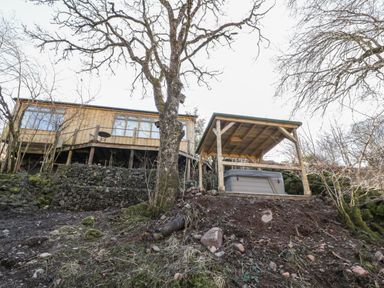A cabin on stilts with a covered hot tub on a hillside surrounded by trees at The River Lodge in Oban