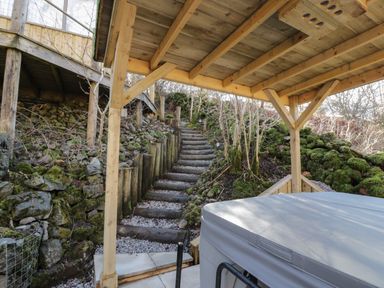 A covered outdoor area with hot tub and wooden stairs leading up a hillside at The River Lodge in Oban