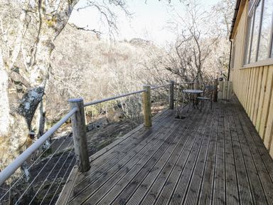 An outdoor wooden deck with railing a table and two chairs attached to a building at The River Lodge in Oban