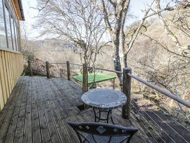 An outdoor wooden deck with a round table and chair surrounded by trees at The River Lodge in Oban