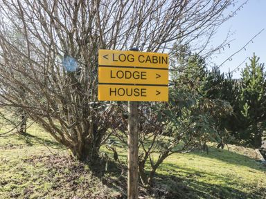 A wooden signpost with directions to log cabin left lodge and house right with trees and grass in the background at The River Lodge in Oban
