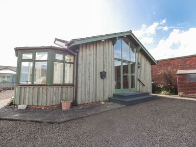 A wooden building with large windows and green frames next to a gravel area at The Shieling in Warkworth