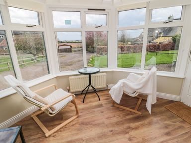 A sunroom with two wooden chairs and a small round glass table between them at The Shieling in Warkworth