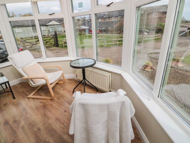 A sitting area with two chairs a small round glass table and large windows showing an outdoor view at The Shieling in Warkworth