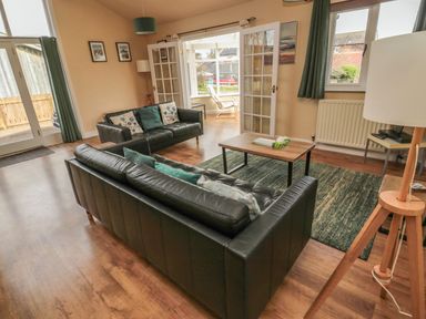A living room with two black leather sofas a wooden coffee table a floor lamp and green curtains at The Shieling in Warkworth