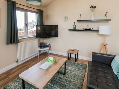 A living room with a black leather sofa wooden coffee table wood floor and shelves on the wall at The Shieling in Warkworth