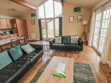 A living room with two black sofas cushions a wooden coffee table a dining table and kitchen cabinets at The Shieling in Warkworth