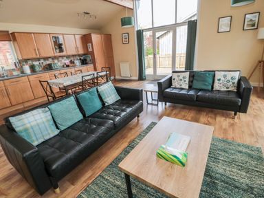 A living room with two black sofas and a wooden coffee table next to a kitchen and dining area at The Shieling in Warkworth