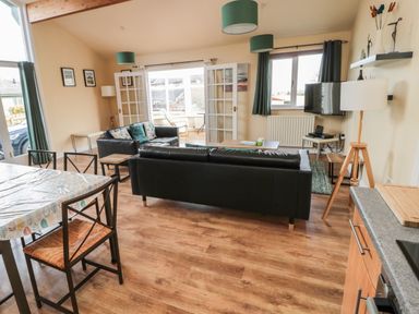 An open living room and dining area with black sofas a dining table with chairs and large windows at The Shieling in Warkworth