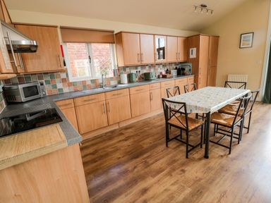 A kitchen with wooden cabinets a dining table with six chairs and kitchen appliances at The Shieling in Warkworth