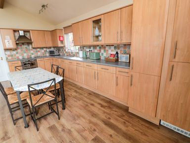 A kitchen with wooden cabinets a dining table with chairs and kitchen appliances at The Shieling in Warkworth