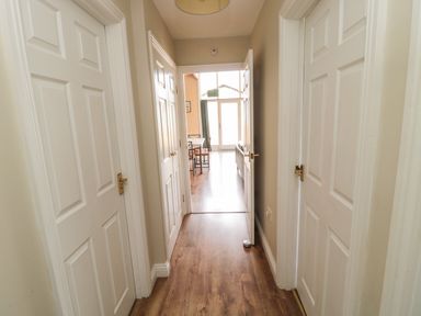 A hallway with wooden flooring and white doors on both sides leading to a room with a dining table and chairs at The Shieling in Warkworth