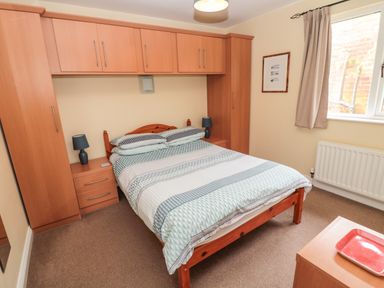 A bedroom with a double bed wooden wardrobes bedside tables lamps and a window at The Shieling in Warkworth