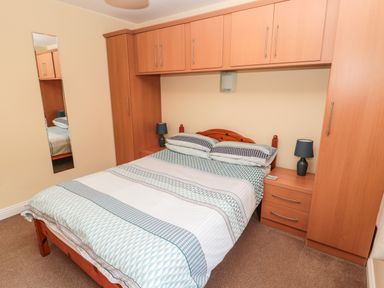 A bedroom with a double bed under wooden overhead cabinets and bedside tables with lamps at The Shieling in Warkworth