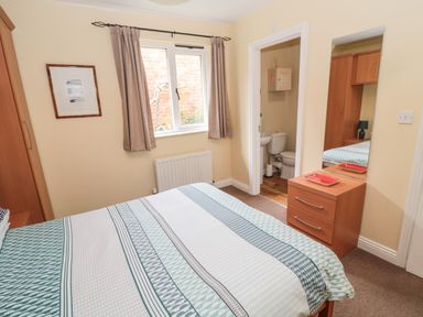 A bedroom with a bed a window a wardrobe a small dresser and an ensuite bathroom at The Shieling in Warkworth