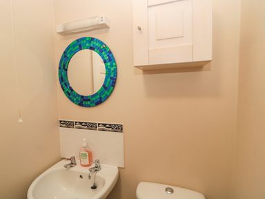A small bathroom with a white sink hand soap blue and green round mirror white wall cabinet and a toilet at The Shieling in Warkworth