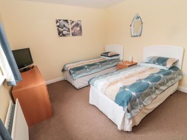 A bedroom with two single beds a wooden dresser with a television and wall art at The Shieling in Warkworth