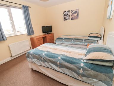 A bedroom with two single beds a wooden dresser with a television on top and a window with curtains at The Shieling in Warkworth