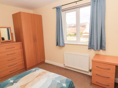 A bedroom with a bed a wardrobe chest of drawers and a window with blue curtains at The Shieling in Warkworth
