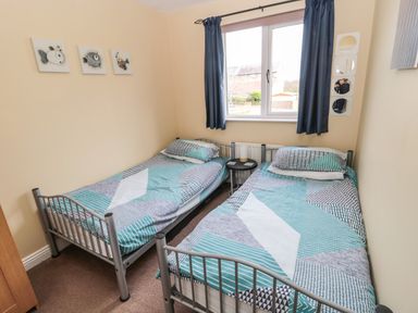 A bedroom with two single beds and a window with blue curtains at The Shieling in Warkworth