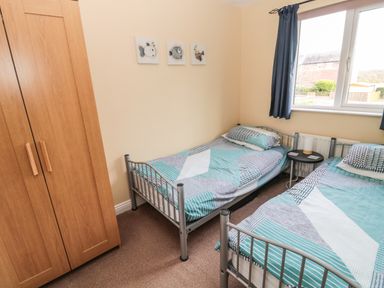 A bedroom with two single beds a wooden wardrobe and a window at The Shieling in Warkworth